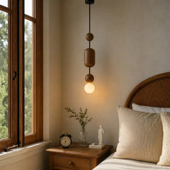 A modern pendant light with a black cord and three stacked wooden cylindrical and spherical shades, glowing with a warm light bulb in a bedroom setting.