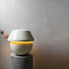 Modern white lamp with a glowing interior on a gray pedestal against a plain background