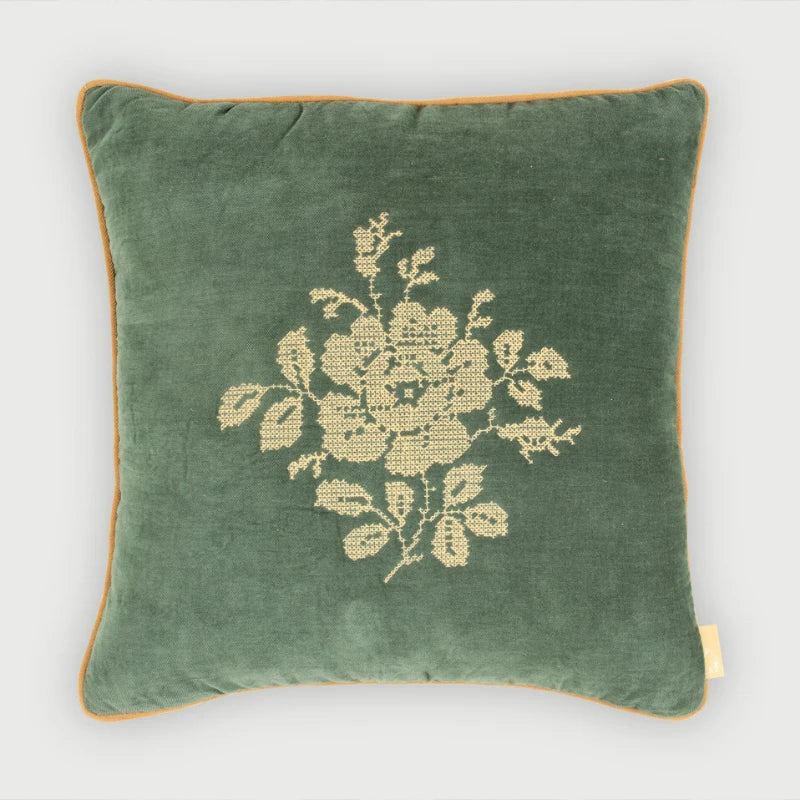 A square green velvet throw pillow with a beige embroidered floral motif in the center and a thin beige piped border, shown against a light gray background.