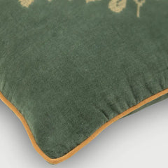 Close-up of a dark green velvet throw pillow with a mustard yellow border trim and a partially visible beige embroidered design.