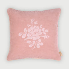 A square pink velvet throw pillow featuring a white embroidered floral motif in the center, set against a clean, light gray background.