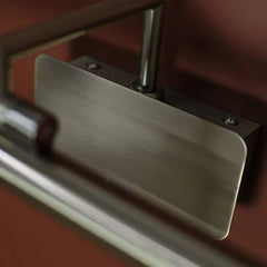 Brass Antique Picture Light, close-up of a brushed metal door pull handle mounted on a dark reddish-brown door, with part of the handle and a metal bar visible.