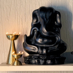 Black decorative Ganesha sculpture on a white surface with gold lamps in the background.