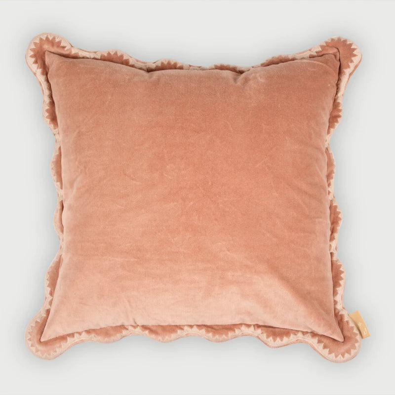 A square blush pink velvet throw pillow with a scalloped edge, shown against a light gray background.
