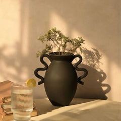 Black Asteria Vase with plant on a table next to a glass of water and lemon slice, soft lighting