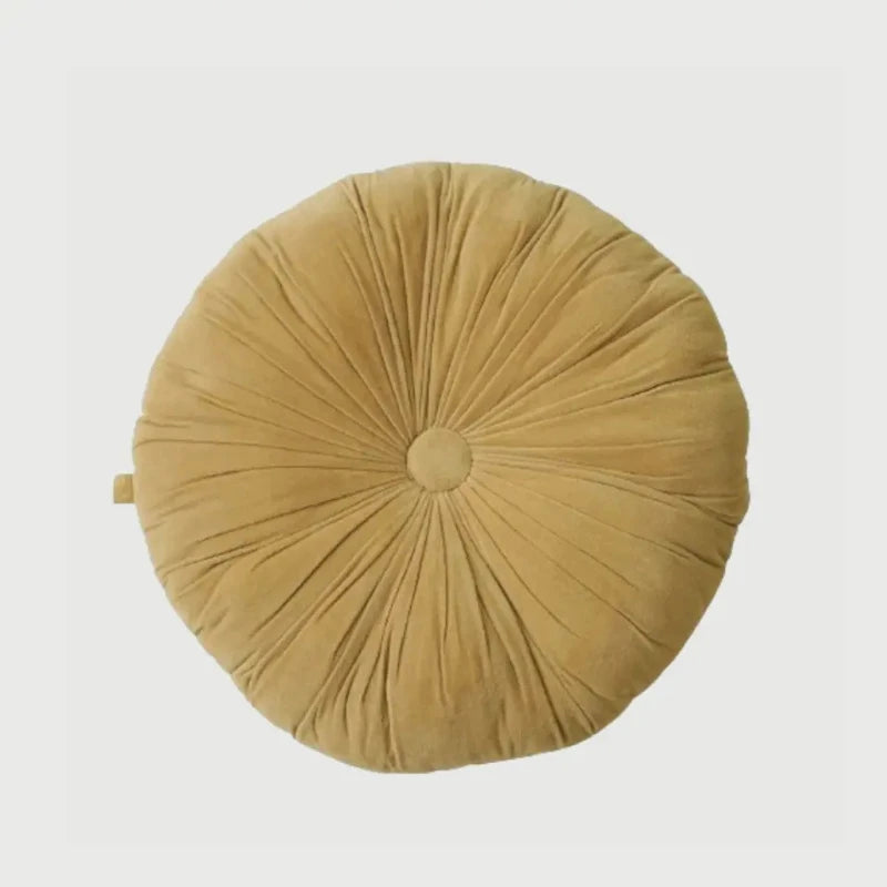 A round, mustard-yellow velvet floor cushion with a central button and radiating pleated folds, shown from a top-down view on a light gray background.