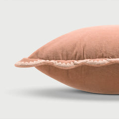 A close-up of a dusty rose velvet throw pillow with a scalloped, hand-embroidered border, shown against a light gray background.