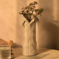 White ceramic solis vase with collar-like rim and hand-textured surface on a beige surface with a warm light background.
