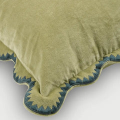Close-up of a plush pillow in a muted olive green velvet fabric, featuring a decorative scalloped edge with blue and green embroidered detailing.