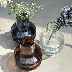 Three different color glass vases with flowers on a reflective surface