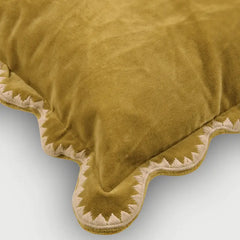 A close-up of a plush velvet throw pillow in a mustard yellow color, featuring a scalloped edge with cream-colored embroidered detailing.