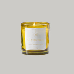 A lit Lily Blossom scented candle in a translucent amber glass jar with a white label reading 'LILY BLOSSOM' .