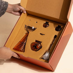 Composite Gift Box opened by hands, tall diya, kalash and bell packed in kraft insert
