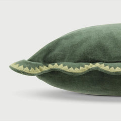 Green velvet pillow with decorative edge on a light gray background
