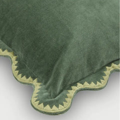 A close-up of a green plush throw blanket with a scalloped edge and a contrasting light beige embroidered pattern.