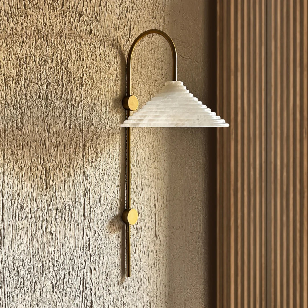 Conical Wall-mounted light fixture with a textured white shade and gold accents on a textured wall.