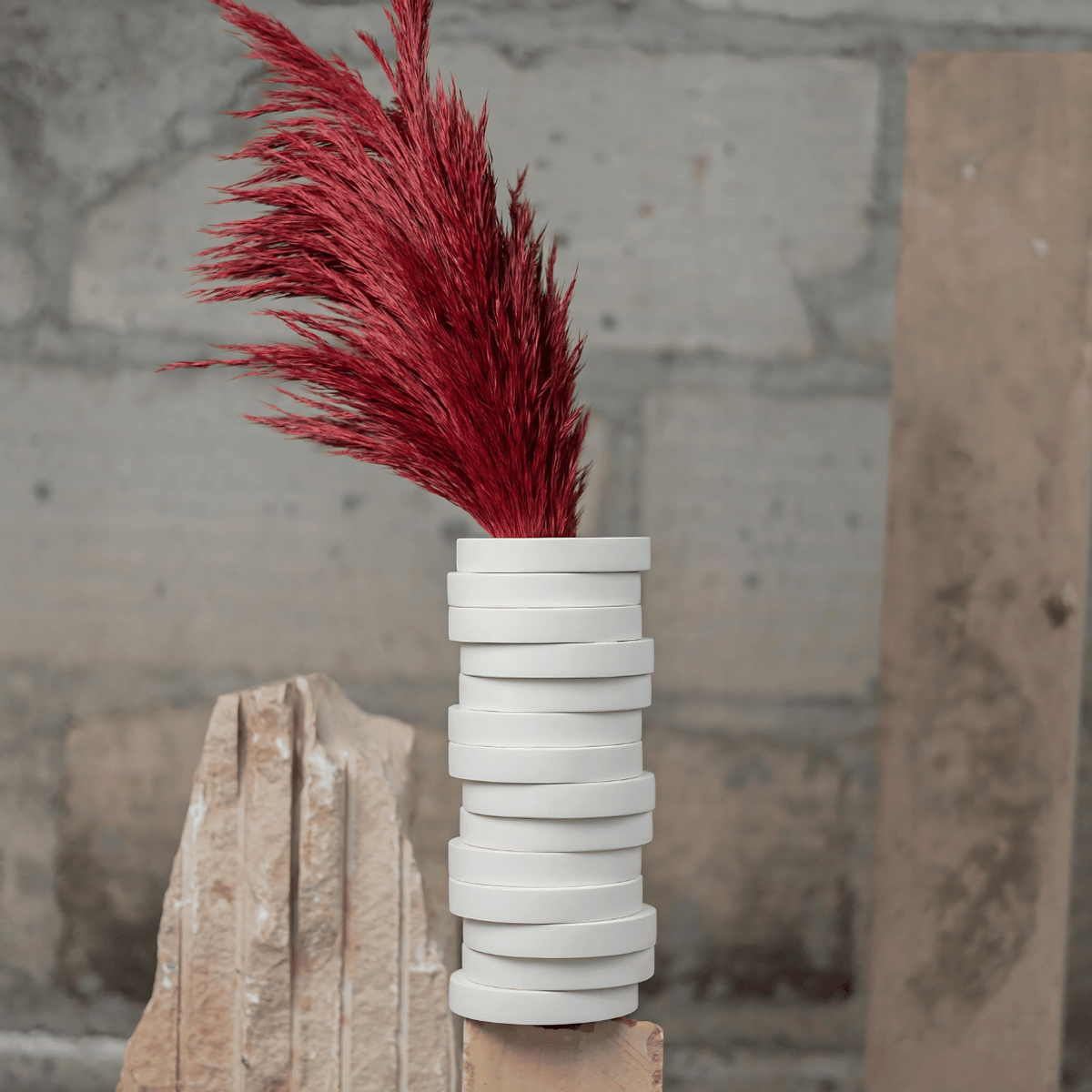 A minimalistic white Yugen vase with stack pieces in white and a red floral-like decoration on top