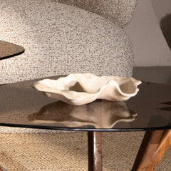 A beige ceramic wavy dish or shallow bowl displayed on a dark glass-topped side table in a living room setting.