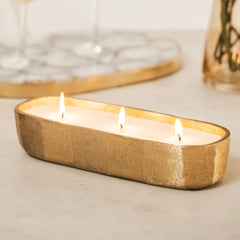 Fleur Votive, gold candle holder with three lit candles on a neutral background