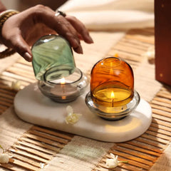 Muun Dome Tealight Holder in teal and amber, hand lifting teal dome off lit base, on white oval tray