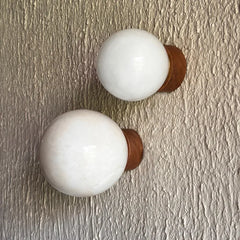 Two styled alabaster wall sconces with large white spherical glass shades and warm brown metal bases, mounted on a textured beige wall.