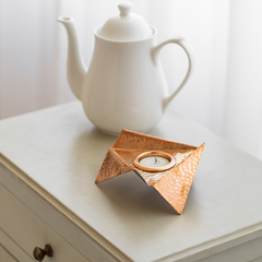 A copper plated brass Origami Tealight - holder with a hammered texture and a candle inside