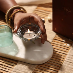 Muun Dome Tealight Holder, hand holding lit slate grey glass base with teal dome at left, angled view