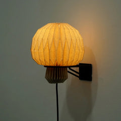 A wall-mounted lamp with a origami-inspired geometric lampshade casting a warm glow, with a sleek black bracket.