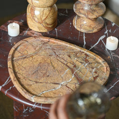Decorative stone tray on a marble table with candles and a candle holder.