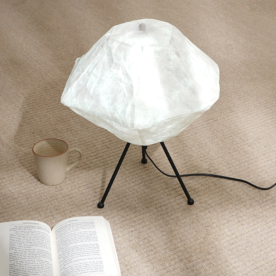 A modern Luna table lamp with a design resembling the moon's surface, mounted on a tripod base, with a braided cable and a foot switch