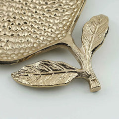 Gold pomegranate shaped Roma tray bottom look with 2 leaves attached on a stem on a light gray background