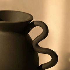 Black ceramic Asteria Vase with a curved handle on a beige background