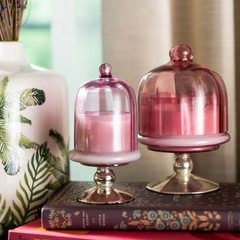 Sundance Aura Candle - Pink, two sizes styled on books beside a leaf-print vase, lifestyle view