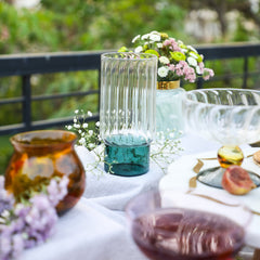 Decorative Highball glass with a striped design and green base placed on white tablecloth with other glass decor items