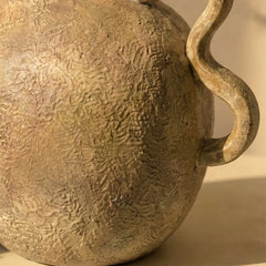 Close-up of a textured ceramic vira vase with a handle on a beige background