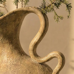 Close-up of a textured vase with a curved handle against a blurred natural background