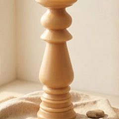 A close-up of a light natural Pillar Candle  (Non Scented) with a fluted, tiered design, resting on a beige linen cloth with a small stone nearby.