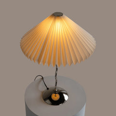 Wavy Table lamp with pleated beige shade, glowing warm light, top view 