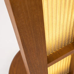 Close-up detail of a wooden furniture piece with a ribbed translucent panel glowing warm yellow light, showing medium brown wood grain and a white background.