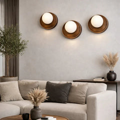 Three modern circular wall sconces with warm bronze-toned metal frames and glowing white globe shades, mounted on a light gray wall above a beige sofa in a styled living room.