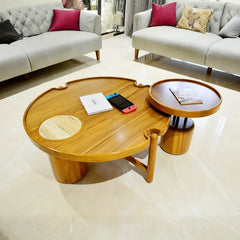 A modern round wooden coffee table with a matching small side stool in a bright, contemporary living room with light gray sofas.