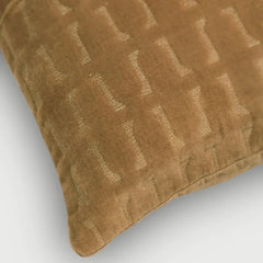 A close-up of a textured Twig Tan Brown Embroidered Velvet Cushion Cover in a warm camel brown color, featuring a subtle woven geometric pattern of interlocking letters on a light gray background.