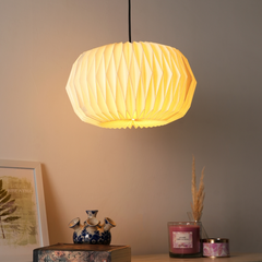 A pendant lamp with a beige origami-style pleated shade, hanging in a room setting with a warm light illuminated.