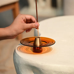 Hand lighting an incense stick over a small round incense burner on a stone surface.