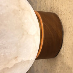Close-up of a spherical white alabaster stone lamp base meeting a cylindrical dark brown wooden or metal socket against a textured beige wall.