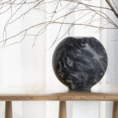 Black marbled vase made of glass on a wooden table with a white curtain background