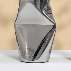 A modern, chrome dented metallic silver vases with a highly reflective, faceted surface and a minimalist 'fig' logo etched near the base, set against a warm beige background.