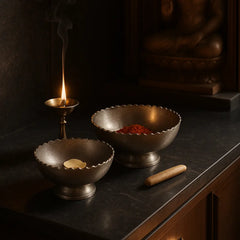 Two metallic bowls made of aluminum in silver finish with a lit candle and incense on a dark surface.