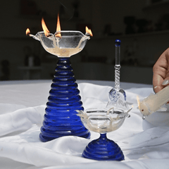 Tall glass diya with blue ribbed pattern in bottom along with short diya and glass ringing bell 
