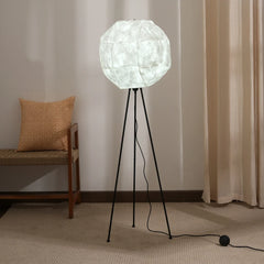 A modern floor lamp with a tripod base and a shade resembling the moon's surface, standing in a room.